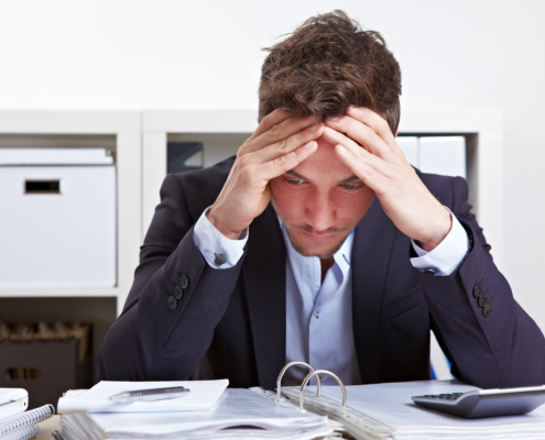 Mann mit Burnout über Akten gebeugt am Schreibtisch im Büro